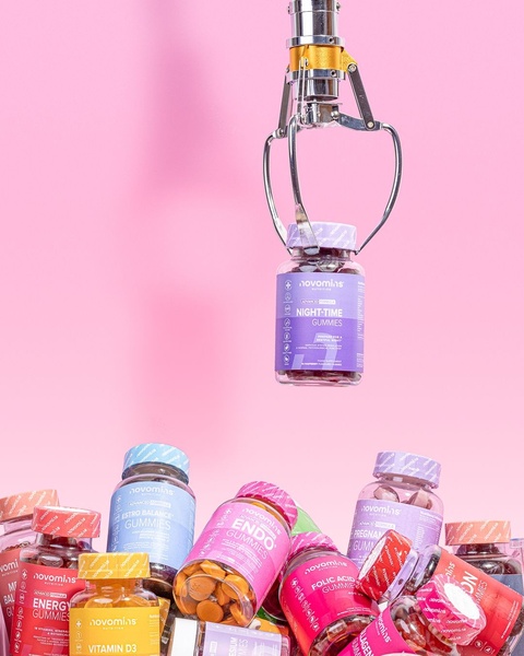 A creative showing a mechanical claw machine selecting a specific bottle of night-time gummy vitamins from a sea of various colorful supplement bottles.